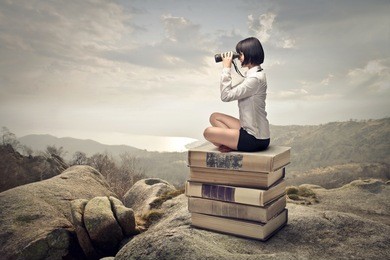 beautiful woman sitting on a pile of old books watching with binoculars