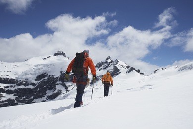 rear view of two hikers joined by safety line in snowy mountains