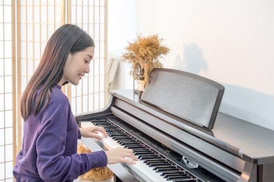 cheerful smiling asian young girl playing piano in sost light. beautiful,happy, joyful, relaxing woman practising piano cheerfully. 