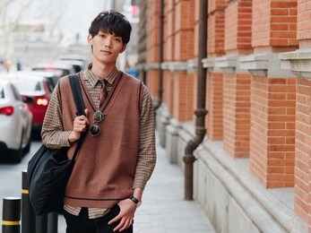 portrait of a handsome chinese young man with korean style clothes walking and looking at camera with sad expression against shanghai street background, male fashion, cool asian young man lifestyle.