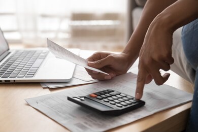 african woman holding paper bills using calculator, close up vie