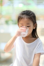 close up asian little girl with white shirt holding glass and drinking water