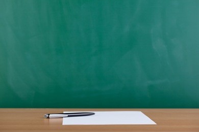 paper and pen ready to be used on desk with blackboard in background