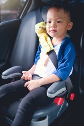 cute little asian 3 - 4 years old toddler boy child sitting in booster car seat, happy traveling, child passenger safety, safe way to travel fastened seat belts in vehicle with young kid concept