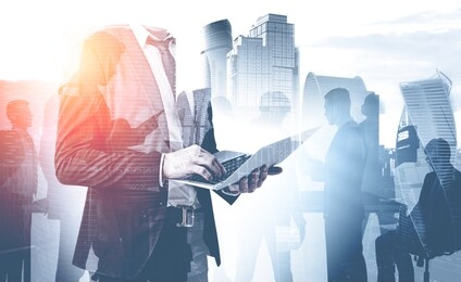 unrecognizable businessman with laptop and his colleague silhouettes over cityscape background. concept of teamwork and business lifestyle. toned image double exposure