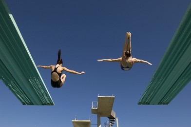 rear view of two women diving from diving boards against clear blue sky