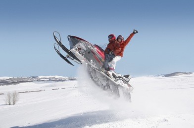 side view of a couple jumping snowmobile in snow