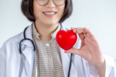 asian woman doctor wearing glasses hold your heart smiling friendly.