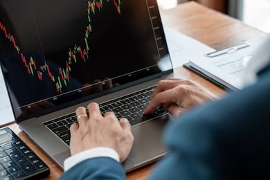 businessman or broker looking at computer laptop analysing about stock market invest trading stocks graph analysis candle line in office room.