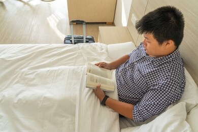 businessman reading book on the bed after being on flight