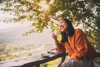 cheerful woman relax drinking tea or coffee in morning with sunshine through the tree background, freedom lifestyle concept
