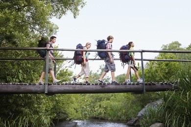 teenage boys and girls with backpacks walking on bridge in forest