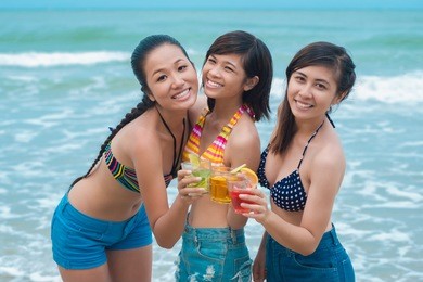 portrait of young girlfriends clicking with cocktails on the beach