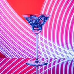 glass with cocktail on the glass table on the neon lights background