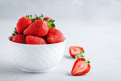 fresh ripe delicious strawberries in a white bowl on a gray stone background
