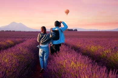 asian couple travel in lavender field in france and take photo a hot air balloon with sun set background.