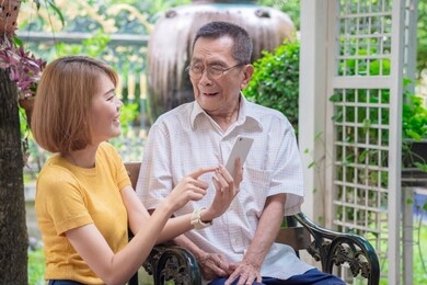 old asian father and daughter. daughter teaches an elderly father to use a mobile phone