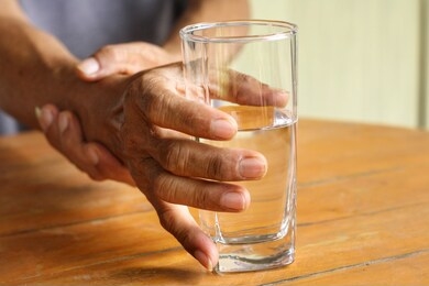 elderly man is holding his hand while drinking water because parkinson's disease.tremor is most symptom and make a trouble for doing activities such as eat or drink.health care or elderly concept.
