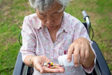 asian senior woman medicine pills or capsules in hand,sick female patient taking,eating vitamin,antibiotic,painkiller,nutritional supplements,elderly people in wheelchair outdoor park,health care 