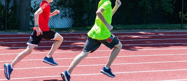 two young boys running fast clockwise on a red track during a track and field running camp.