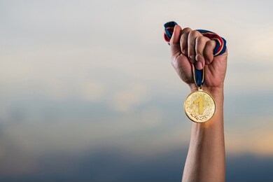 hand holding gold medal on against cloudy twilight sky background, the winner and successful concept 