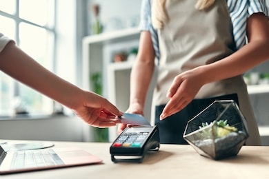 female florist in flower shop. young beautiful blonde selling flowers and succulents. cropped image of customer paying using credit card