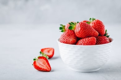 fresh ripe delicious strawberries in a white bowl on a gray stone background