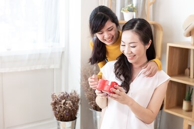 happy asian family teenage daughter give gift box to her mom in a room with nature sunlight at home. show love, happy mother's day concept