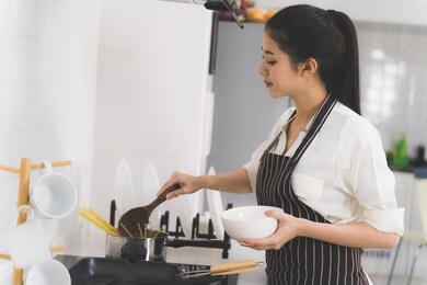 beautiful asian woman or housewife is cooking food for family in white kitchen