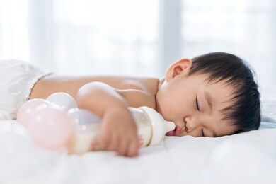 baby sleeping on a bed after drinking bottle milk