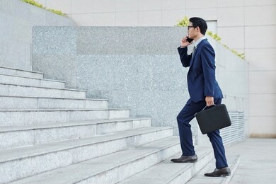 confident successful vietnamese entrepreneur walking up the stairs and talking on phone with coworker