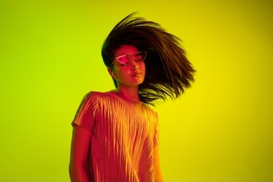 beautiful female half-length portrait isolated on yellow studio background in neon light. young emotional woman. human emotions, facial expression concept. dance in eyeglasses and wireless headphones.