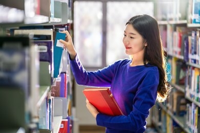 asian young student in casual suit searching the book from book shelf in library of university or colleage with various book background, back to school concept