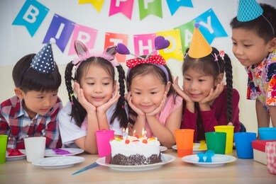 group of asian kids looking at candle on cake at birthday party
