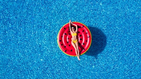 aerial view of female in bikini lying on a floating mattress in swimming pool, inflatable mattress watermelon toy in swimming pool water from above, summer vacation concept background