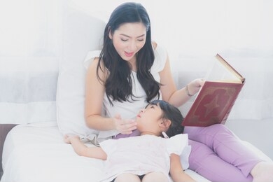 happy mother and daughtermother reading a book to her daughterin bed together to enhance child development and learning to read relaxing in bedroom enjoy bedtime stories