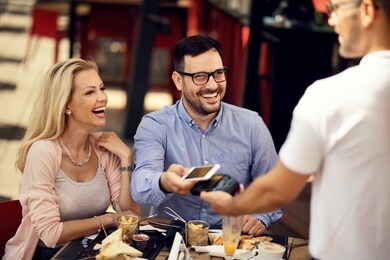 happy couple having fun while making contactless payment via smart phone in a bar. 