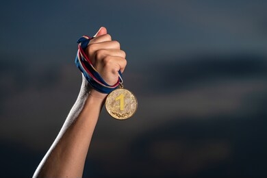 hand holding gold medal on against cloudy twilight sky background, the winner and successful concept 