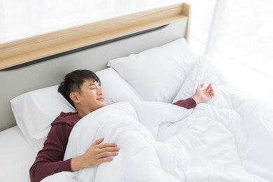 close up shot of asian handsome man lying on comfort bed, he slept deep in bedroom.