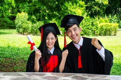a man and woman couple dressed in black graduation gown or graduates with congratulations with hold diploma in hand is sitting