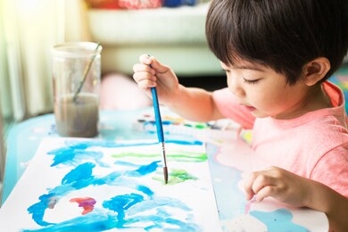 asian cute boy drawing watercolor on white paper floor indoors.