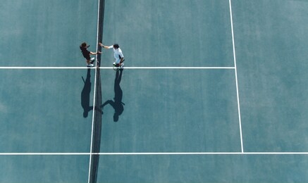 aerial shot of professional tennis players handshakes at the net. sportsmen shaking hands over the net on hard court.