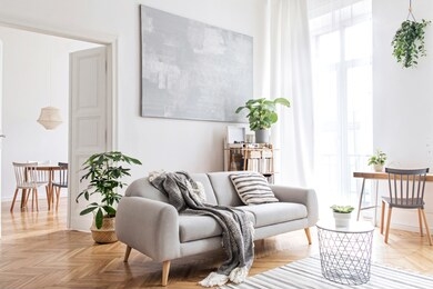 stylish scandinavian living room with design furniture, plants, bamboo bookstand and wooden desk. brown wooden parquet. abstract painting on the white wall. nice apartment. modern decor of bright room