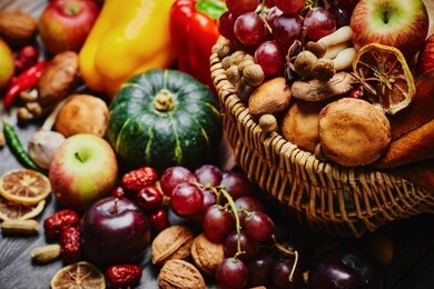 autumn still life. different fruits and vegetables in the wicker basket on the wooden table: pumpkin, grape, garlic, apple, nuts, peanuts, drain, bell peppers,  hot pepper and dry lemon slices  table 