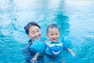 happy asian family, young active asian mother and adorable little toddler boy having fun in a swimming pool,child learning to swim and enjoying summer vacation at a tropical resort.copy space.