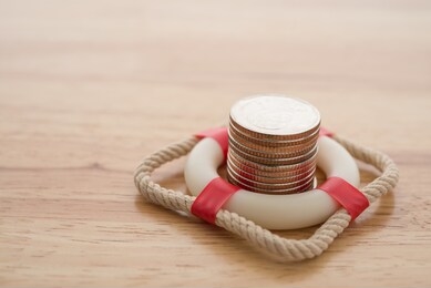 stacked coins in red lifebuoy or lifebelt with wooden background copy space. assets wealth, money saving or money investment protection and security by insurance concept. risk management analysis.