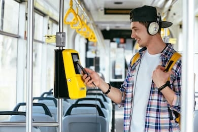 everyday life and commuting to work or study by bus tram concept. handsome student man with headphones listening music and paying transport ticket with mobile phone.