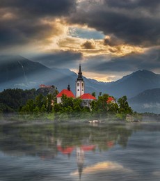 bled, slovenia - misty sunrise at lake bled (blejsko jezero) with the pilgrimage church of the assumption of maria on a small island and bled castle and julian alps at background on a foggy morning