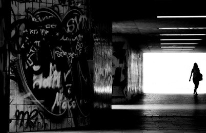a pedestrian crosses a dark, tiled tunnel with graffiti on the walls/in the dark tunnel               