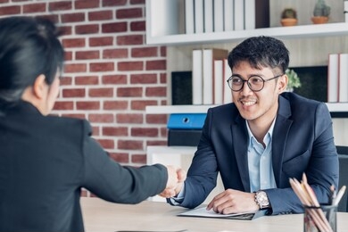 young asian businessman and businesswoman handshake about business agreement at meeting table in modern office.business partnership concept.satisfied the deal with client negotiation